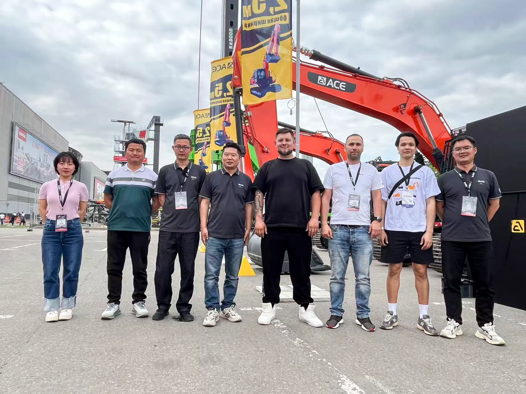 The ACE Group team posing with international clients in front of an orange excavator, demonstrating global trust and strong customer relationships ahead of CTT 2026.